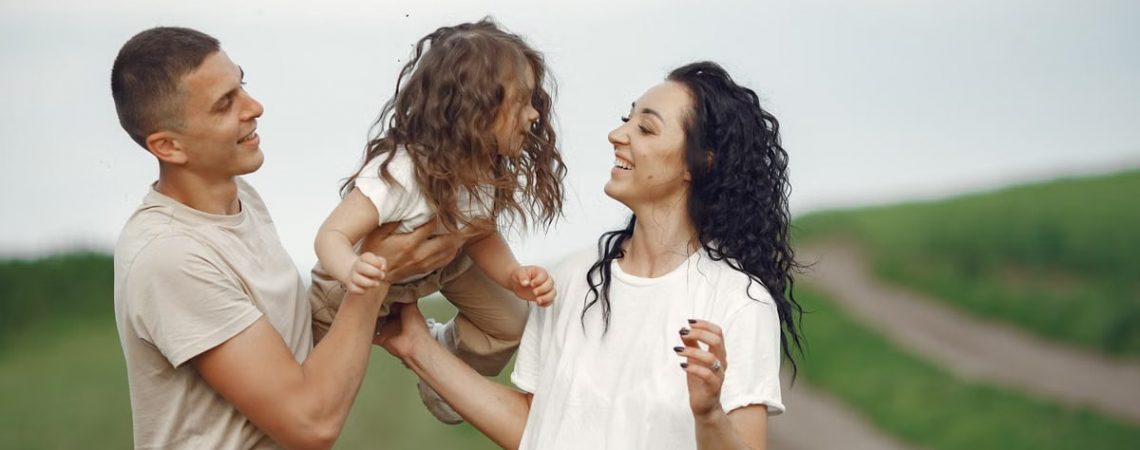 A joyful family moment outdoors with parents playing with their daughter.